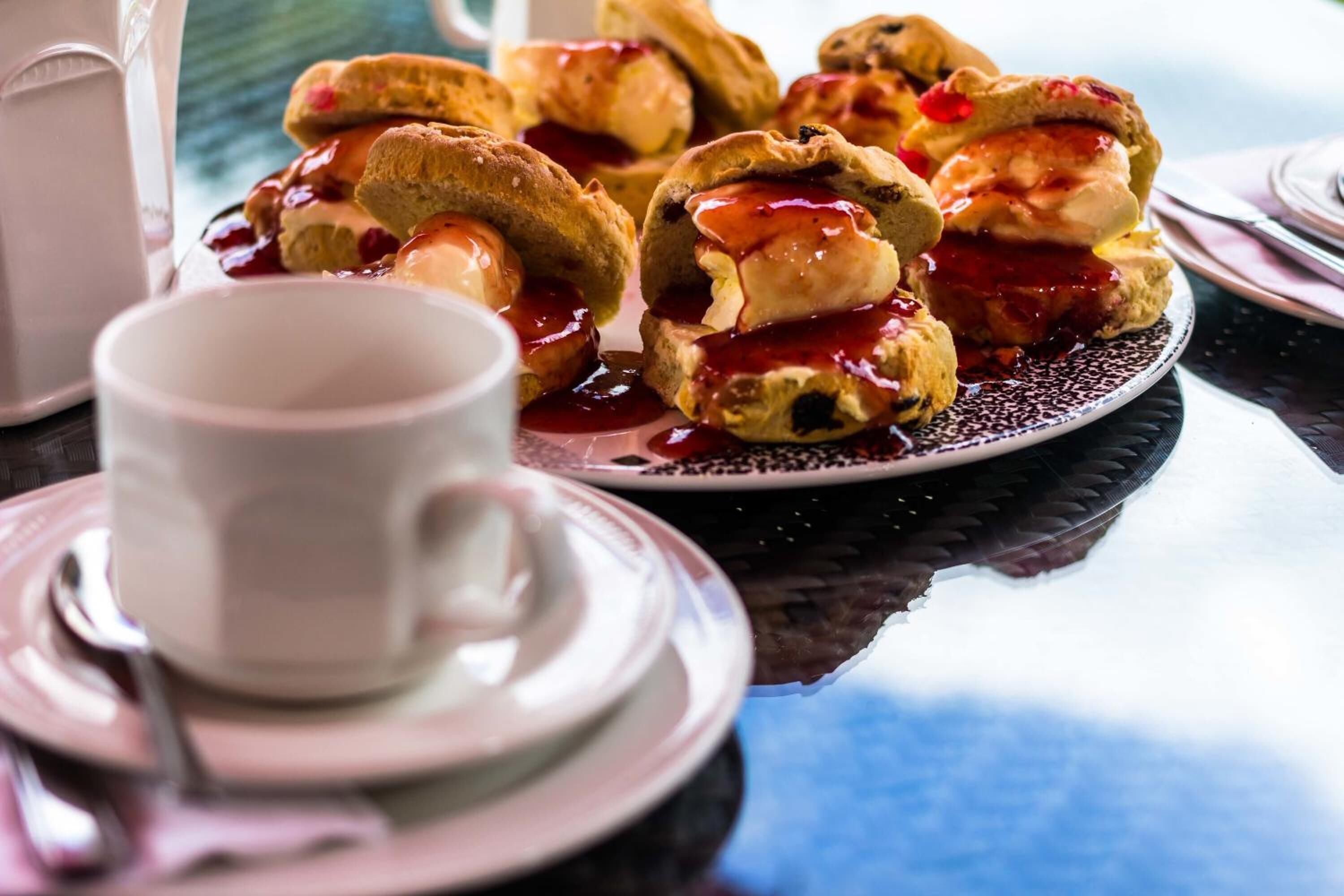 Une assiette de scones accompagnés de confiture et de crème, une tasse blanche et une soucoupe, le tout posé sur une table.