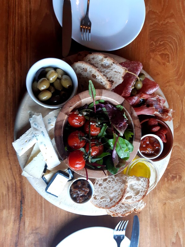 A wooden table with a charcuterie board featuring various cheeses, olives, tomatoes, and meats.