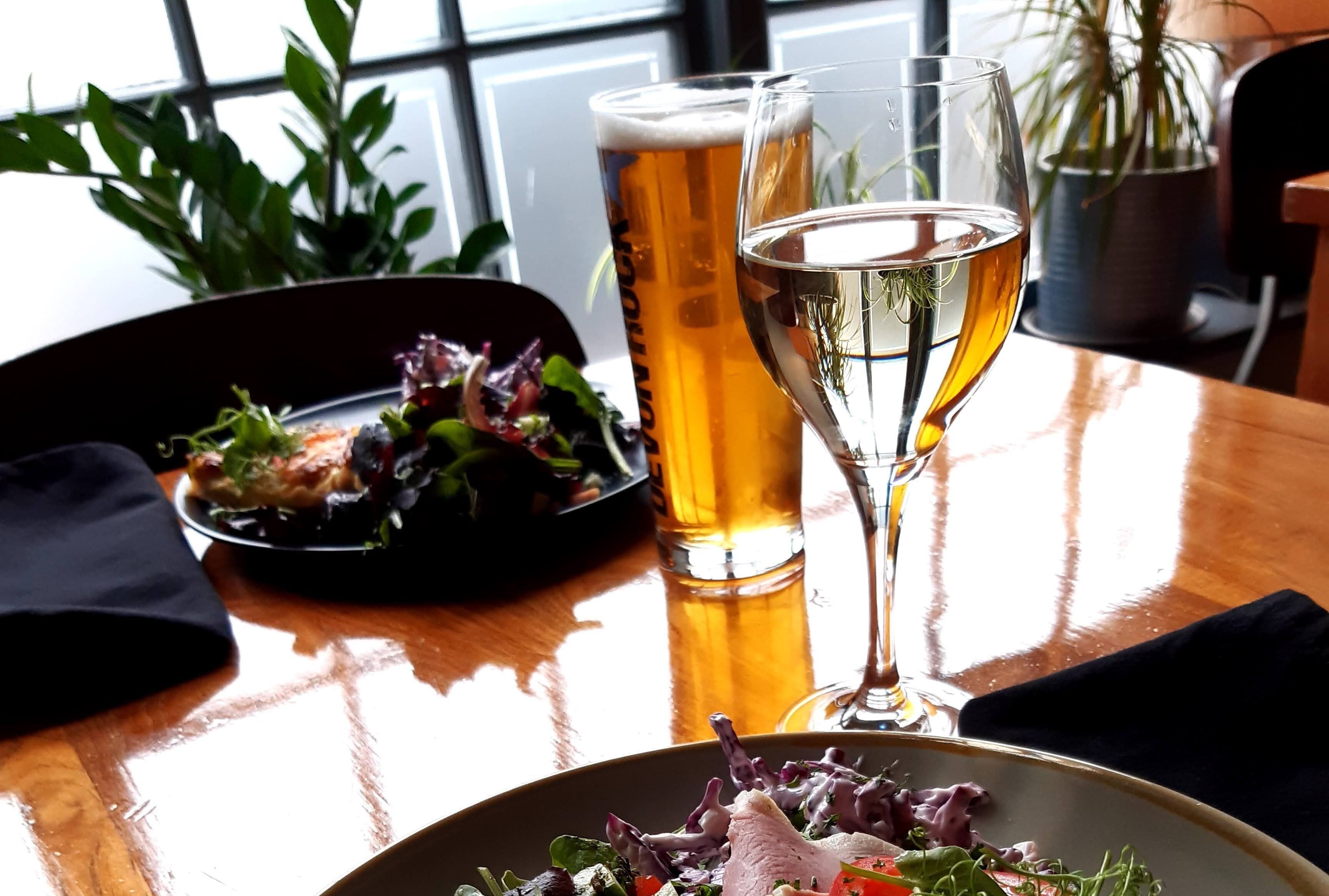 Ein Tisch mit einem Salat, zwei Biergläsern und einer Zimmerpflanze im Hintergrund.