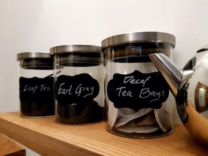 Three glass jars with metal lids labeled 'Leaf Tea', 'Earl Grey', and 'Decaf Tea Bags' on a wooden shelf.