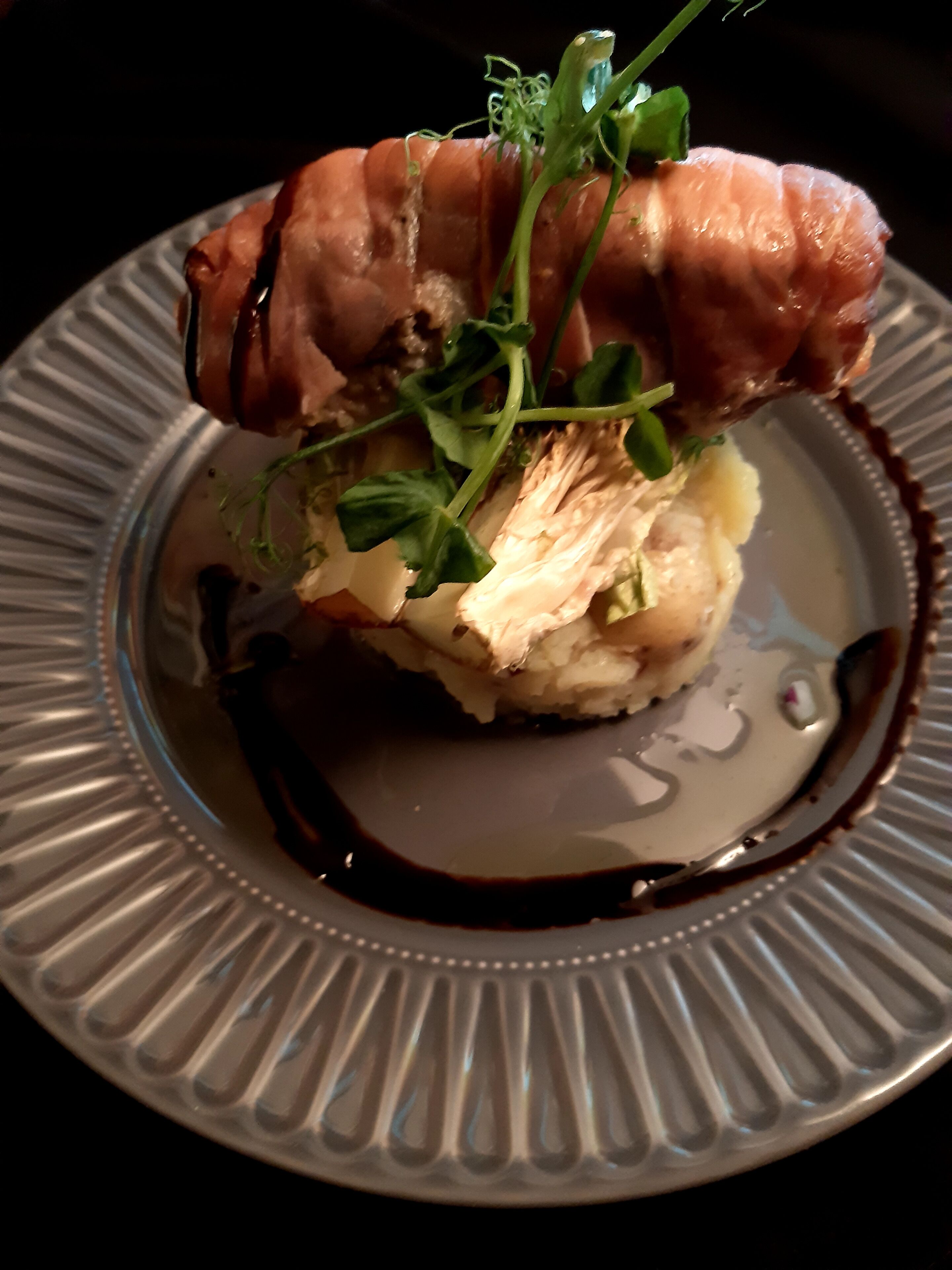 A plate with a dish consisting of a pastry, greens, and a sauce.