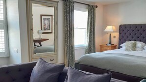 Ein Hotelzimmer mit Bett, Sofa, Sessel, Nachttisch mit Lampe und einem Fenster mit Vorhängen.