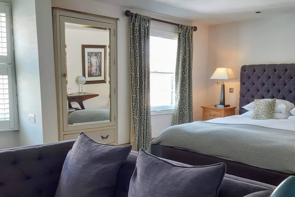 Une chambre d’hôtel comprenant un lit, un canapé, une chaise, une table de chevet avec une lampe et une fenêtre avec des rideaux.