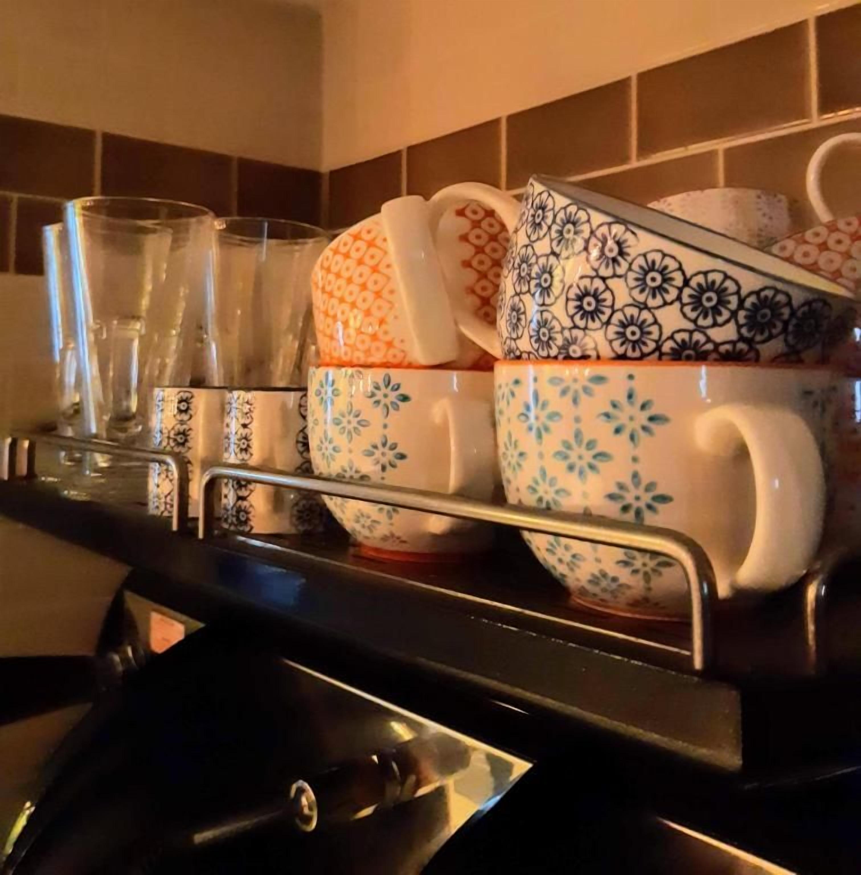 Una encimera de cocina con un hervidor, una pila de tazas y una bandeja con vasos.