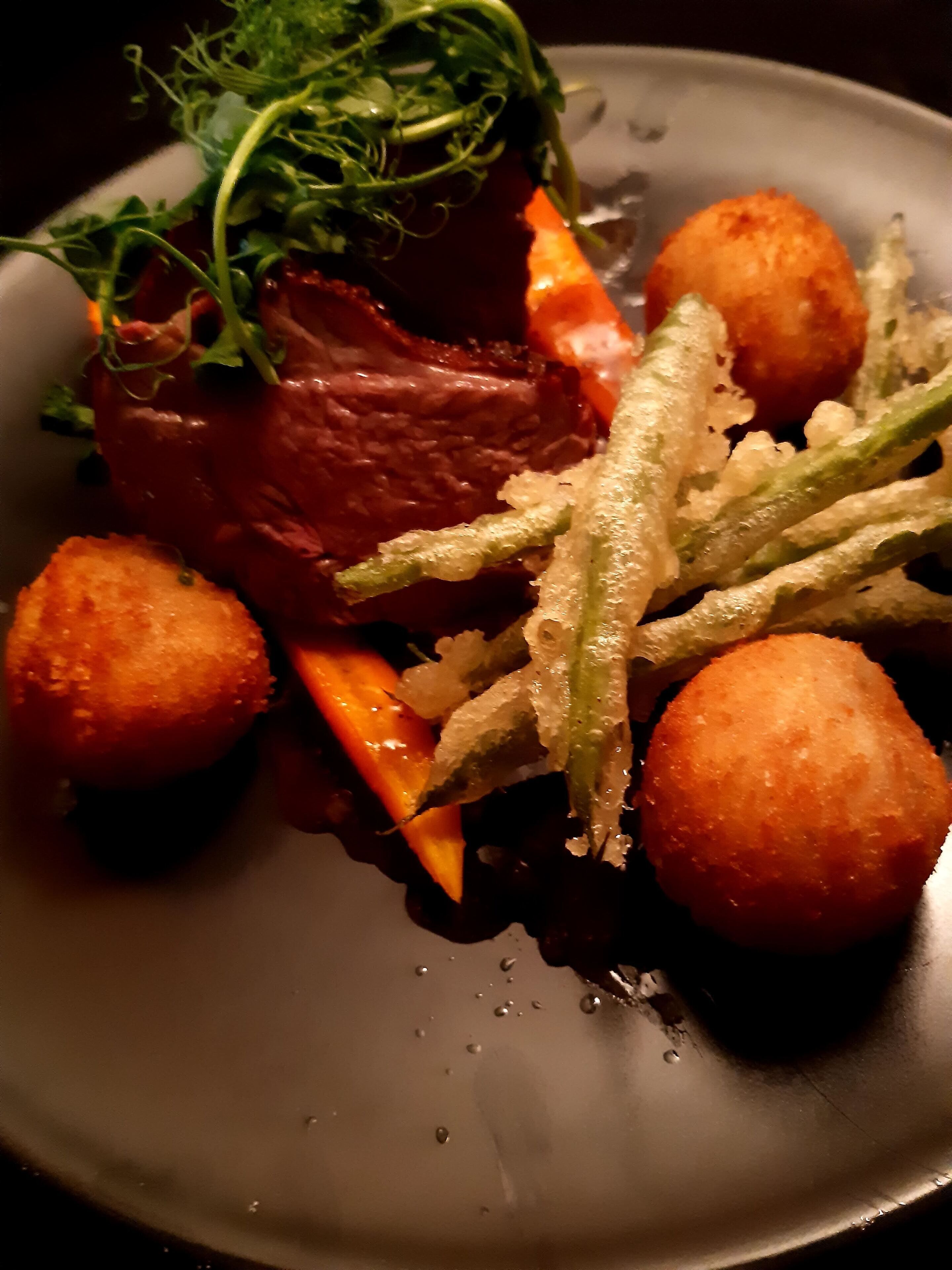 A plate of food with a piece of meat, vegetables, and two round items.