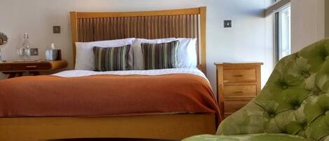 A hotel room with a bed, bedside table, lamp, and a green upholstered chair.