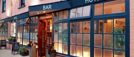 A hotel with a bar and restaurant on the ground floor, featuring large windows and a welcoming entrance.