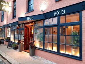 Un hôtel doté d’un bar et d’un restaurant situés au rez-de-chaussée, avec de grandes fenêtres et une entrée accueillante.