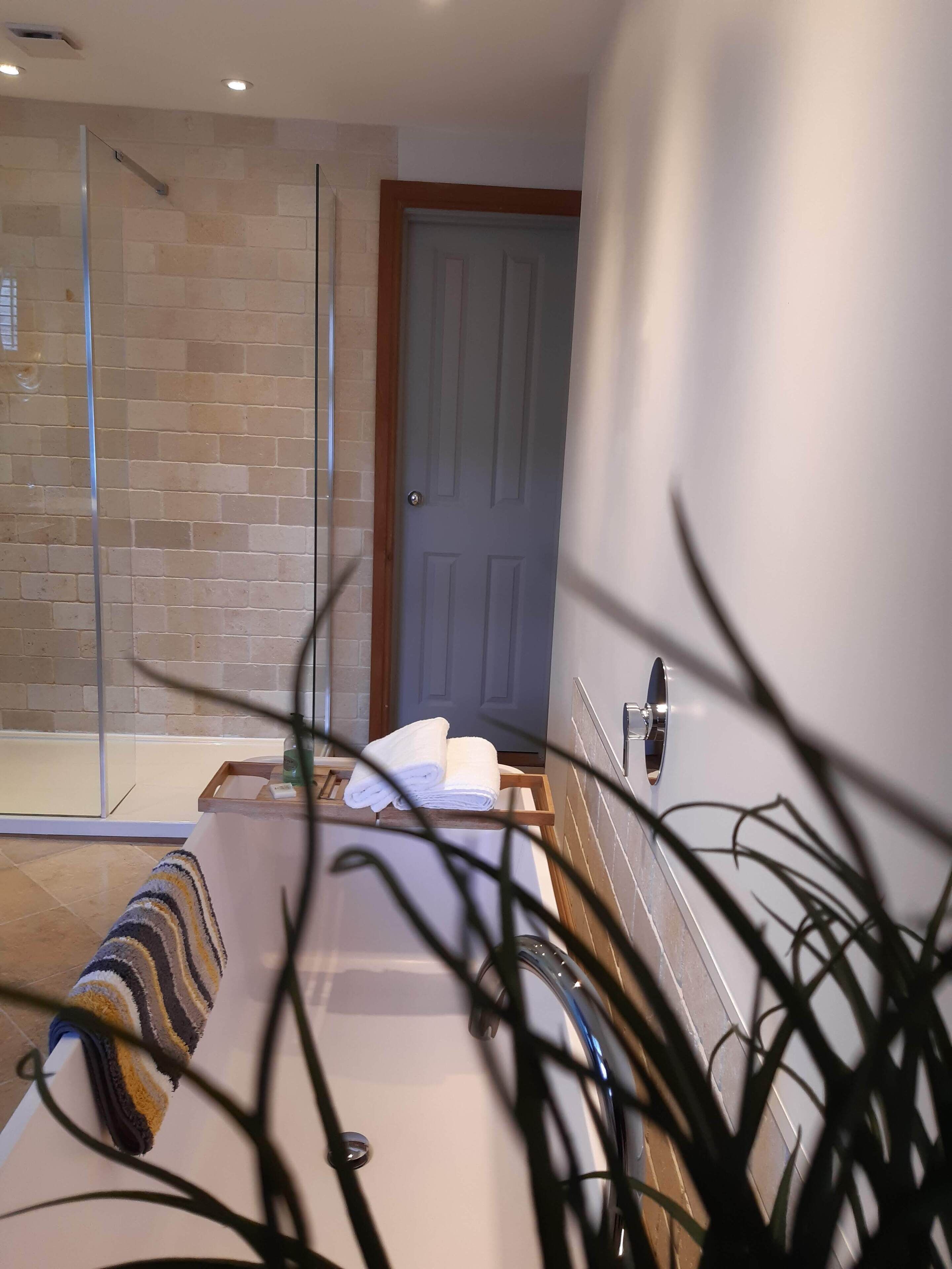 A hotel room with a glass shower enclosure, a wooden bench with towels, and a door with a wooden frame.