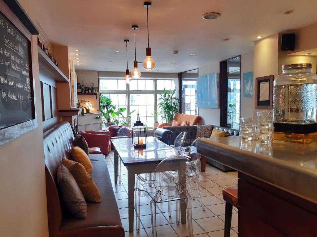 A modern bar area with a seating arrangement, a chalkboard menu, and a large window providing natural light.