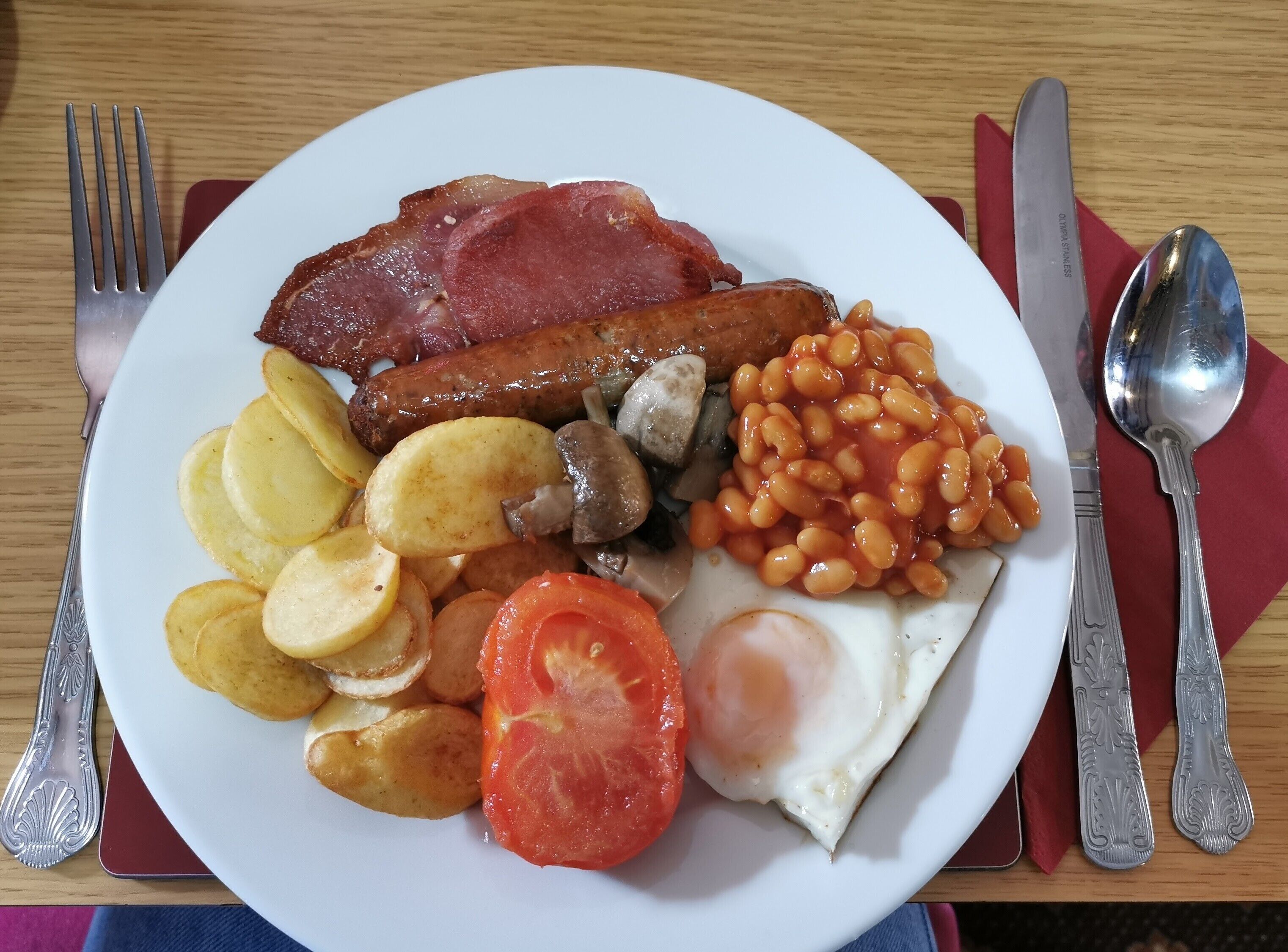 Un plato de desayuno con salchichas, tocino, huevos, frijoles, champiñones y tomates.