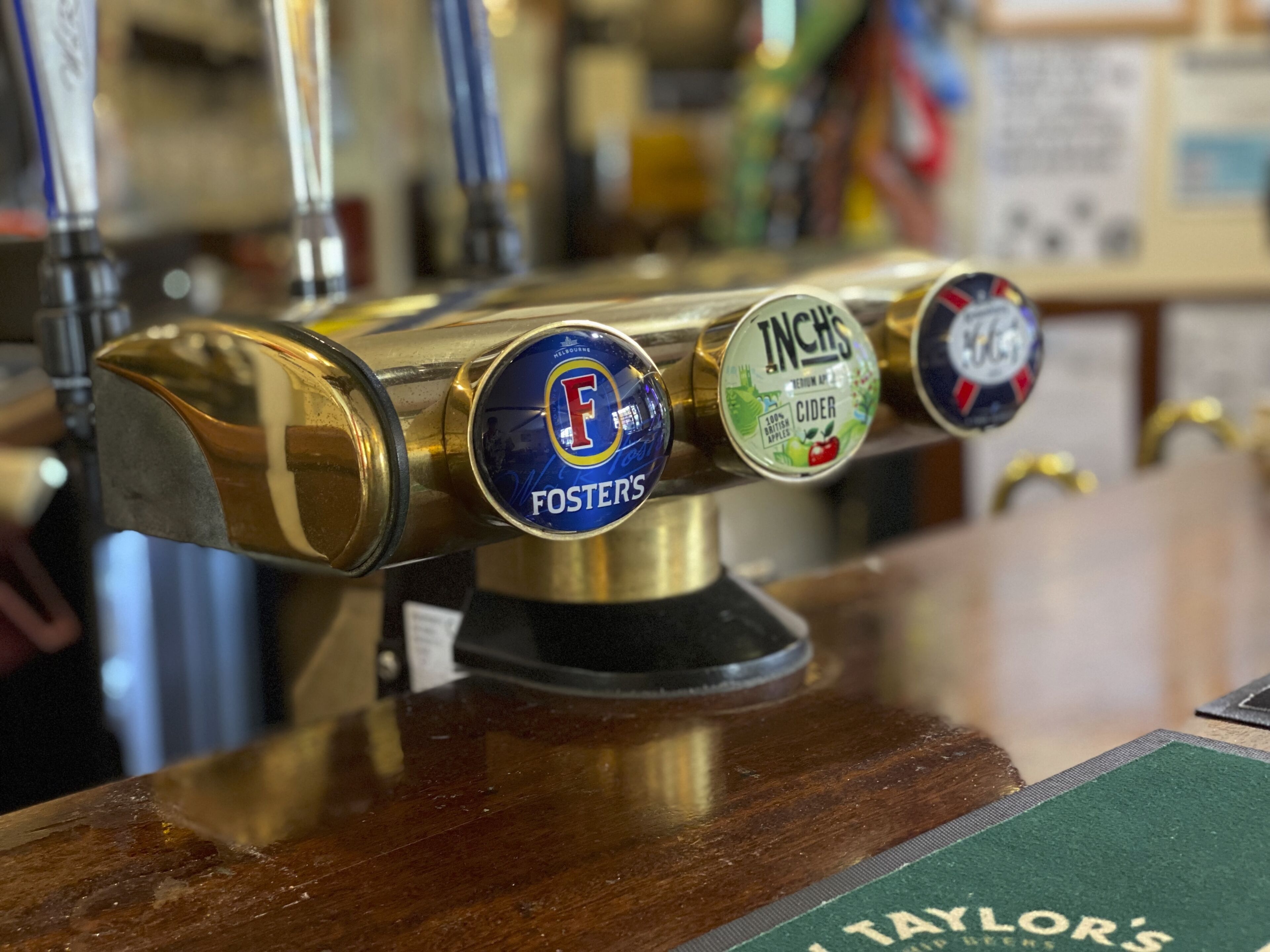 Un grifo con tres etiquetas de cerveza: Fosters, InChs y una tercera etiqueta con un diseño rojo y blanco.