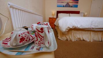 A hotel room with a bed, a bedside table with a tray of breakfast items, a radiator, and a painting on the wall.