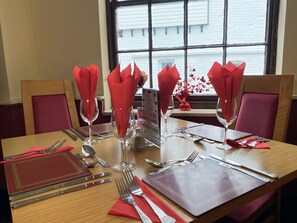 Een gedekte eettafel met rode servetten, bestek en heldere wijnglazen, met een menukaartstandaard en een uitzicht op een raam op de achtergrond.