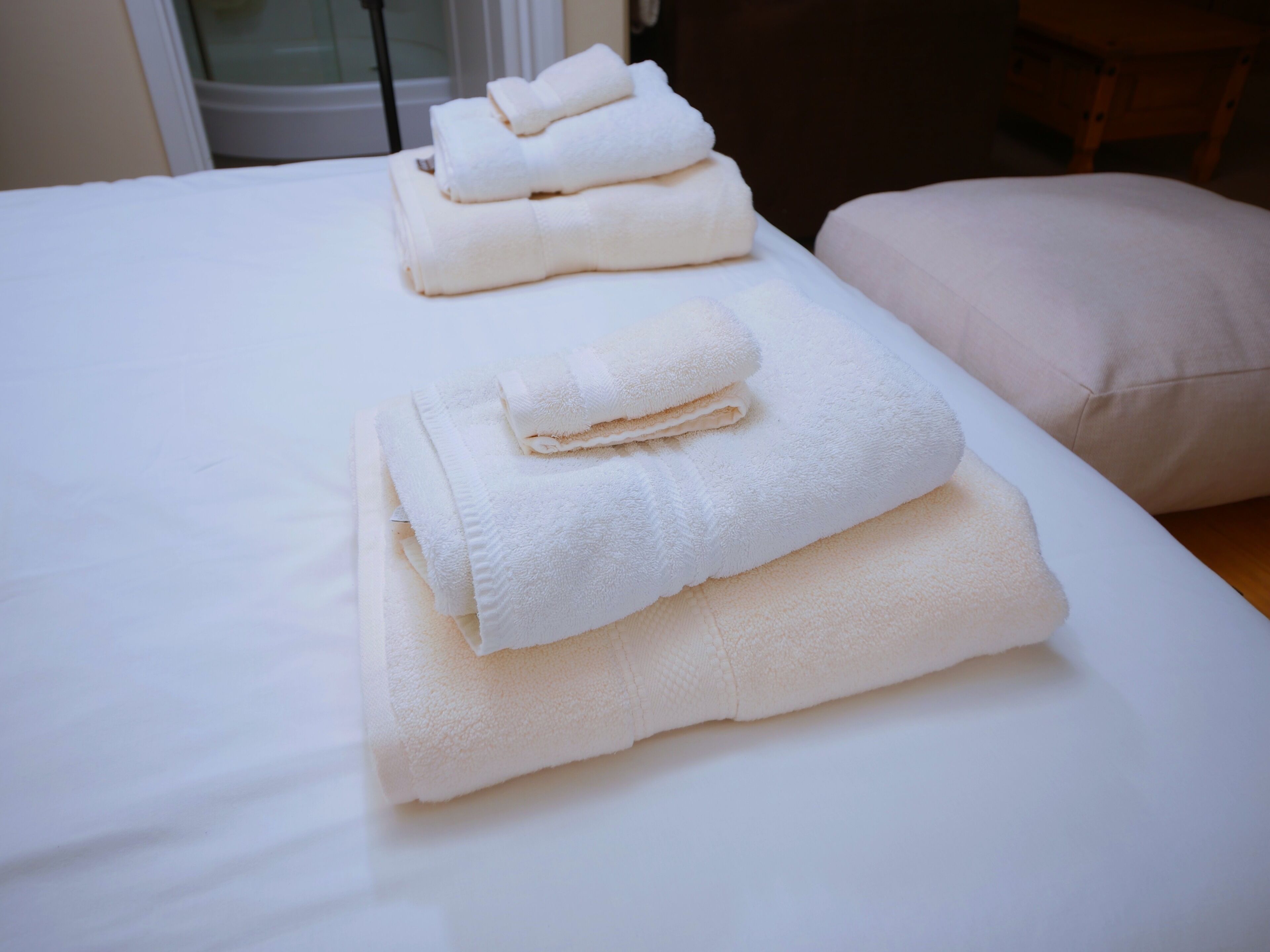 A neatly made bed with white linens and two folded towels stacked on top.
