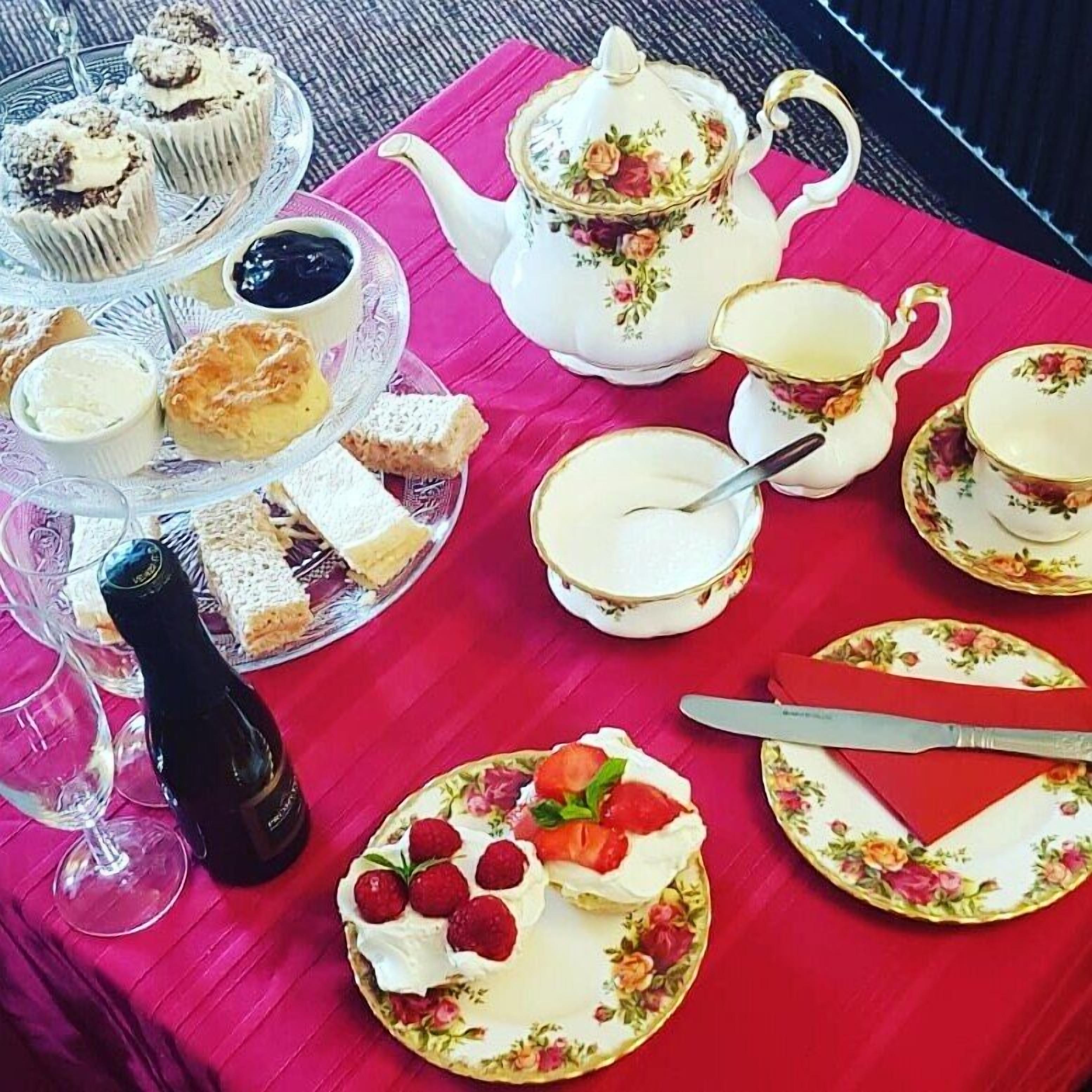 Une table dressée avec un service à thé, des sandwichs, des scones et un gâteau aux fraises et aux framboises.