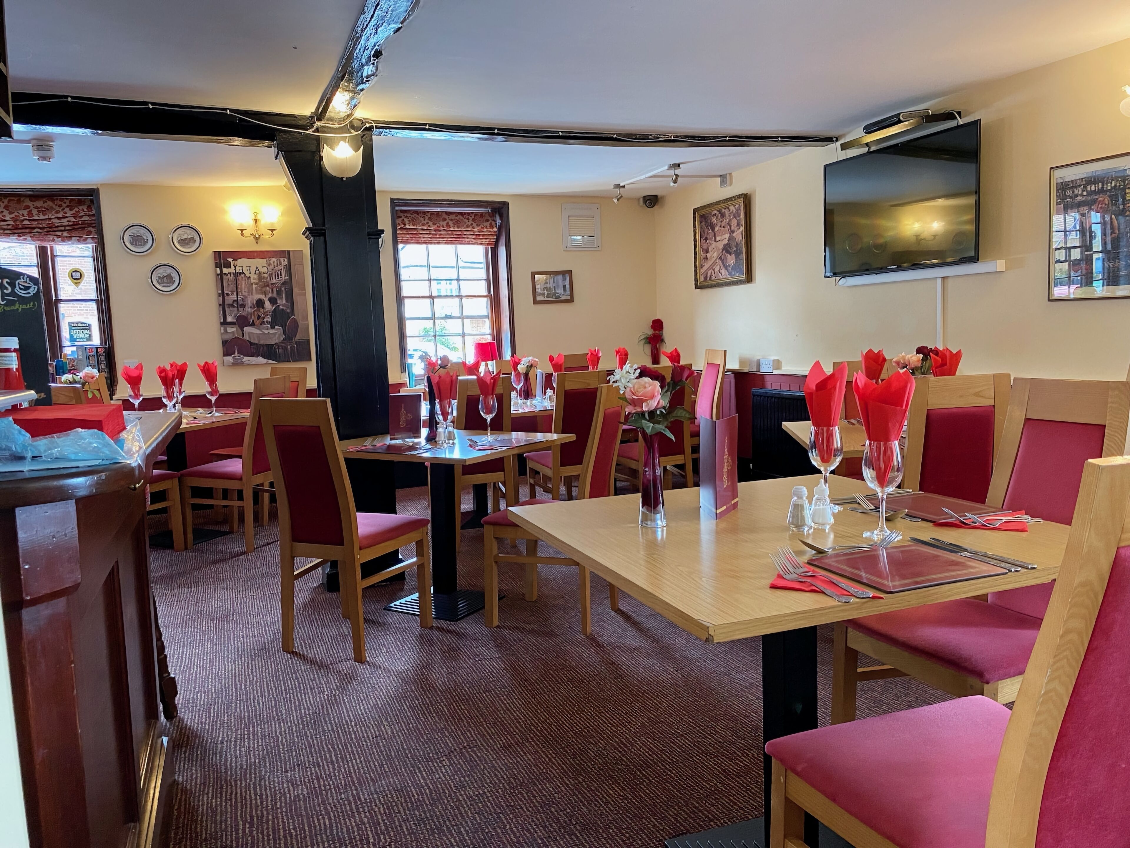 Un restaurante con mesas de madera y sillas tapizadas rojas, decorado con servilletas rojas y arreglos florales.