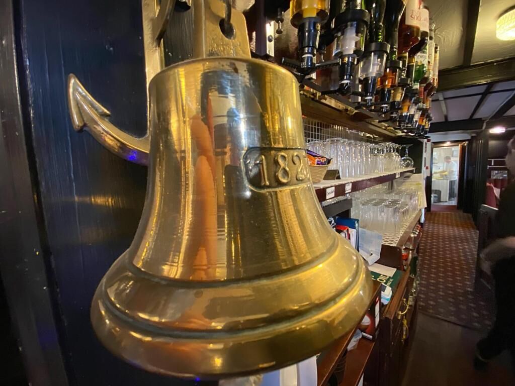Una campana de bronce con el número 182 en una barra de bar.