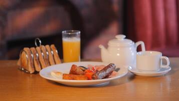 A breakfast setting with a plate of sausages, toast, and a glass of orange juice.