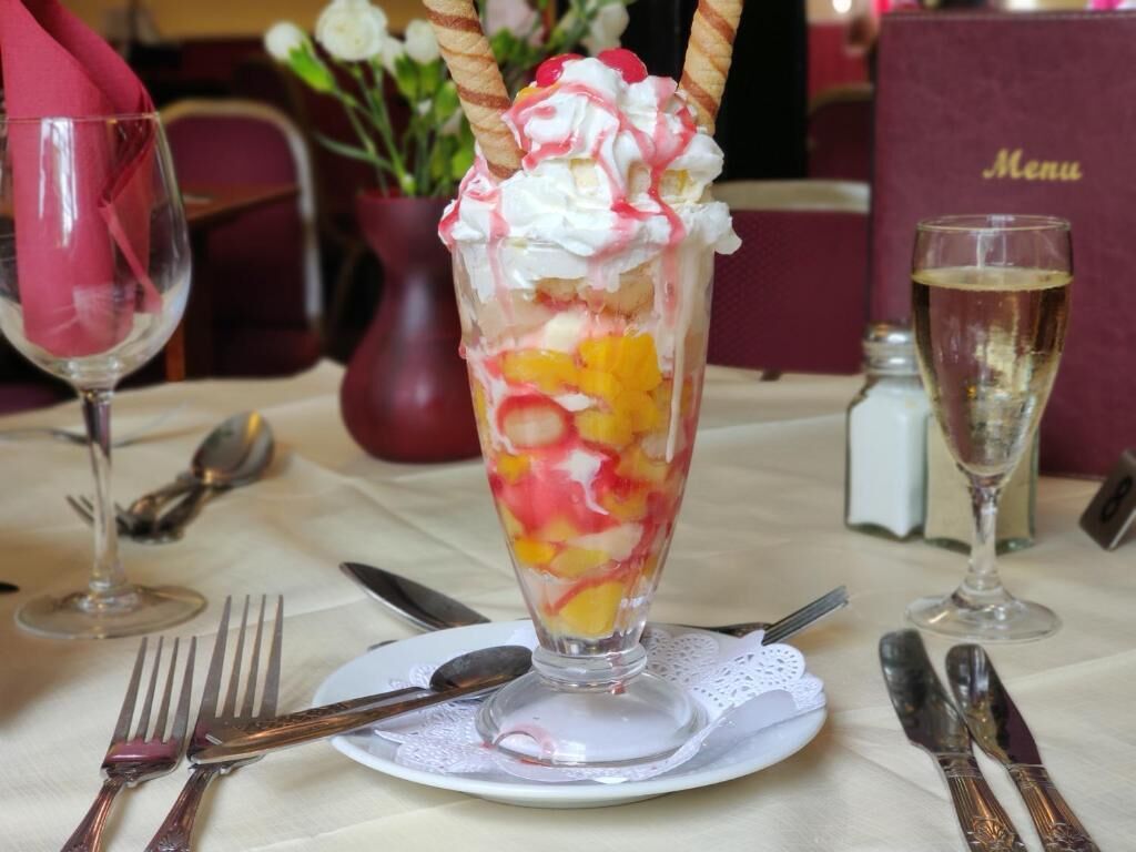 A dessert in a tall glass on a table with cutlery and a menu in the background.