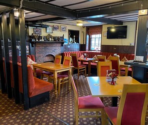 Een restaurant met houten tafels en rode, beklede banken, een open haard van baksteen en een flatscreen televisie aan de muur.