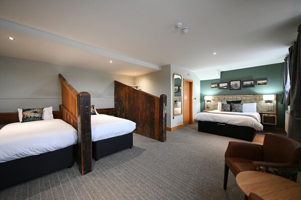 A hotel room with two beds, a wooden staircase, a mirror, a nightstand, and a chair.
