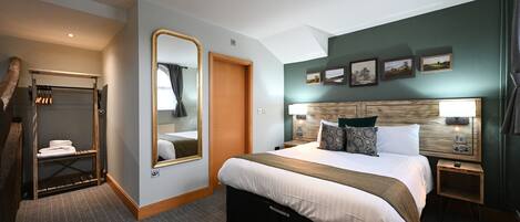 Habitación de hotel con una cama grande, un cabecero de madera, una mesita de noche con lámpara, un espejo y un armario.