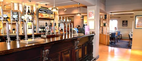 Un espace bar doté de plusieurs robinets à bière et d’un comptoir. On y trouve des étagères remplies de bouteilles et, au fond, un panneau affichant le menu.