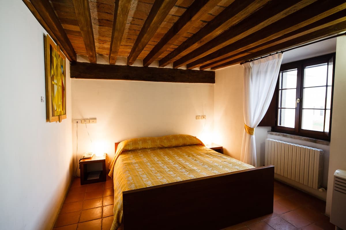 Ein Schlafzimmer mit einem hölzernen Bettgestell, einem Nachttisch mit Lampe, einem Heizkörper und einem Fenster mit Vorhängen.