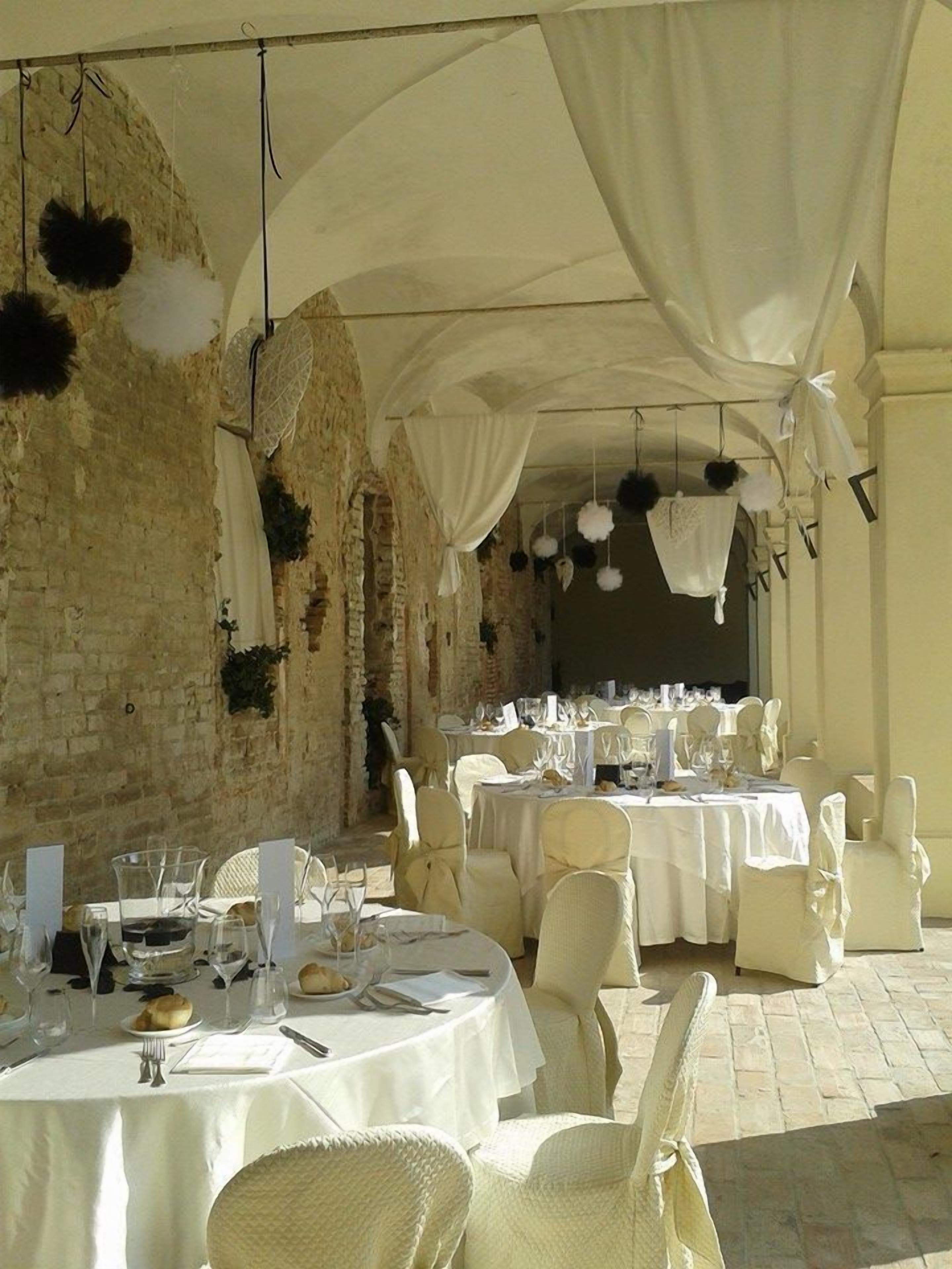 Zona pranzo all'aperto con tavoli e sedie bianche, sullo sfondo di una rustica parete in pietra.