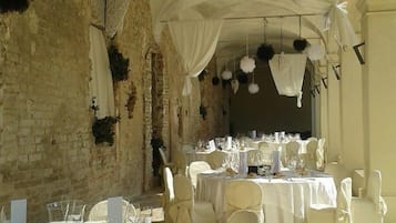 Zona pranzo all'aperto con tavoli e sedie bianche, sullo sfondo di una rustica parete in pietra.