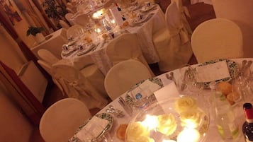 Un salón de banquetes con mesas redondas dispuestas para un evento formal, con manteles blancos, centros de mesa florales y cubertería ordenada.