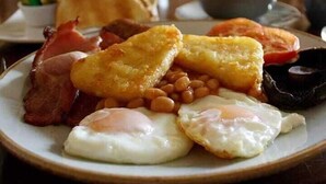 Une assiette de nourriture pour le petit-déjeuner comprenant des œufs, du bacon, des haricots et des bananes plantains frites.