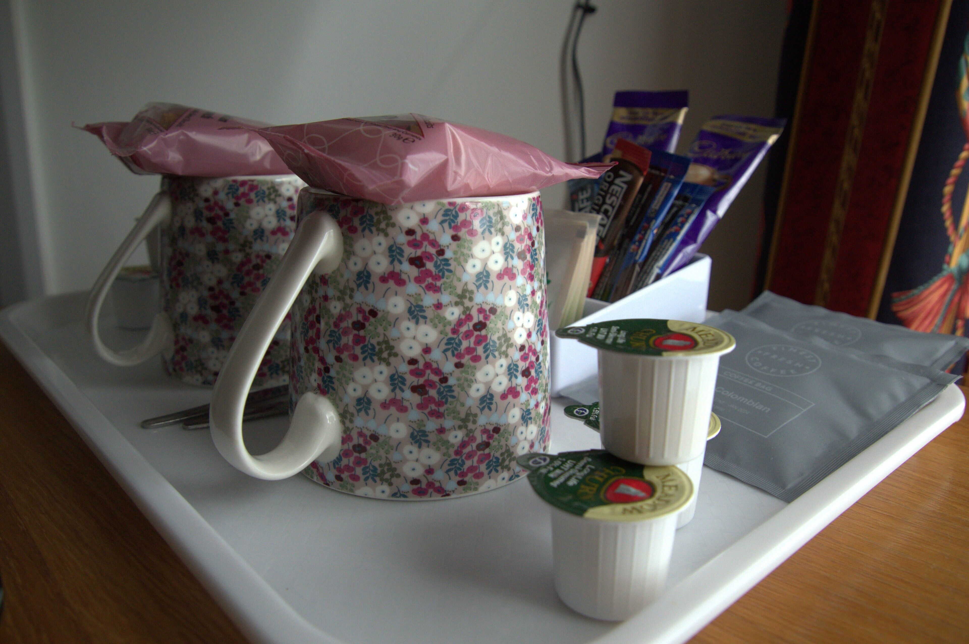A tray with a floral mug, a white mug, and some packets on a table.