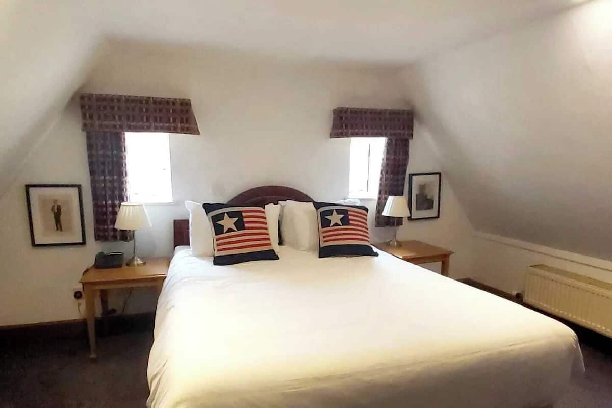 Une chambre à coucher bien rangée, avec un grand lit, deux tables de chevet et des rideaux.