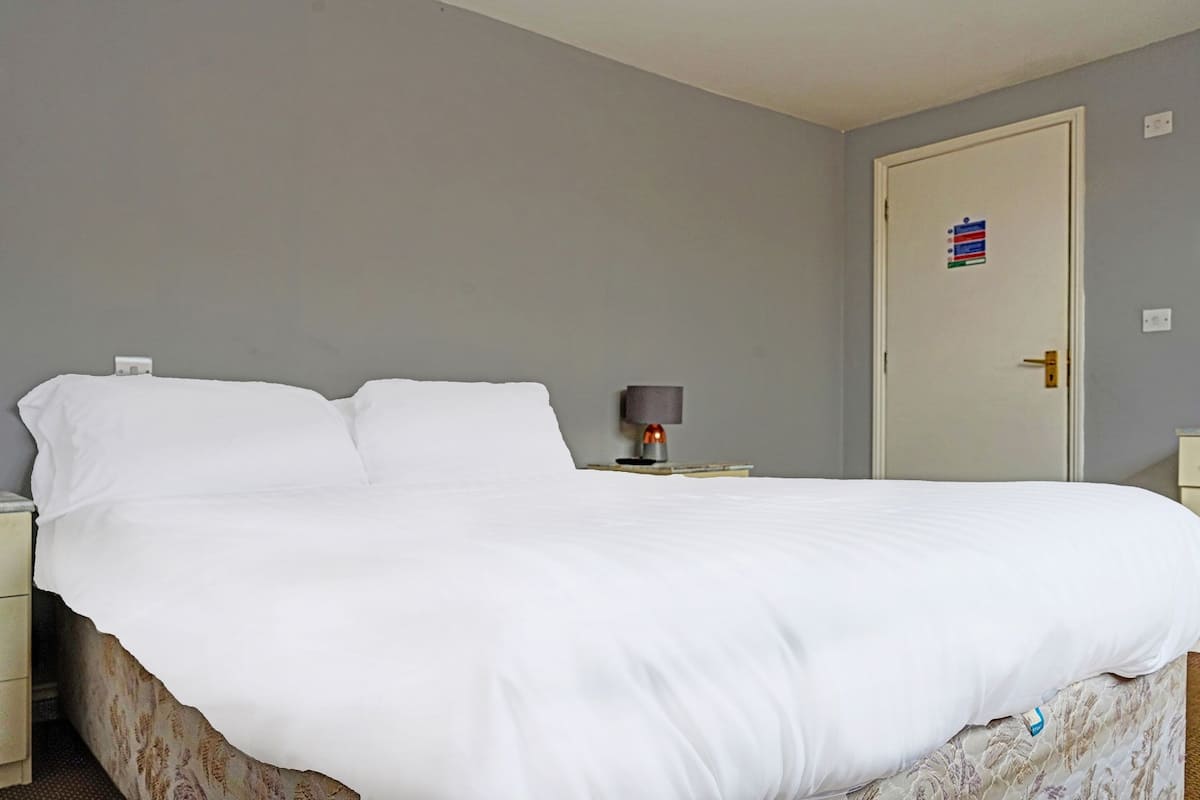 A neatly made bed with white linens, a bedside lamp, and a door with a small sticker.