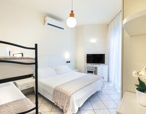 A hotel room with a bed, a desk, a chair, a TV, and an air conditioning unit. - Hotel Fenice (Cervia)