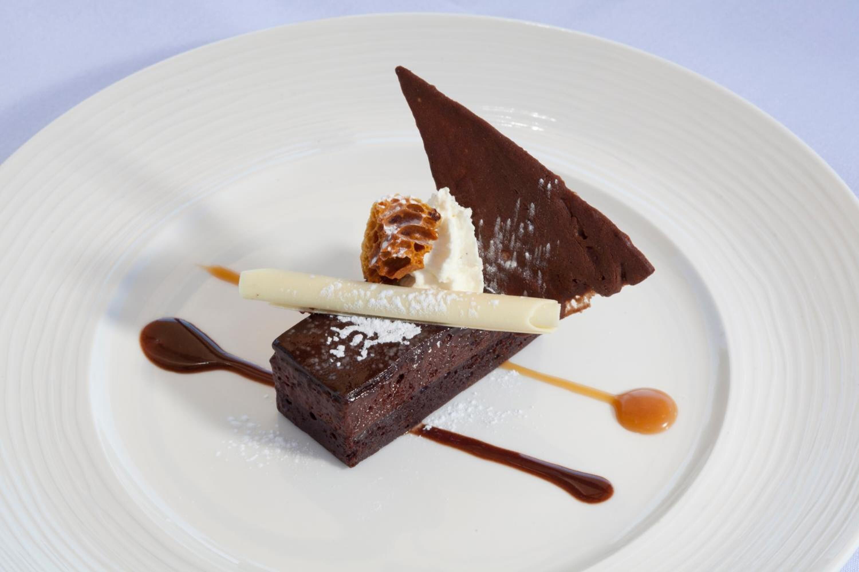 A dessert on a white plate with a chocolate piece, a caramel drizzle, and a white cream.