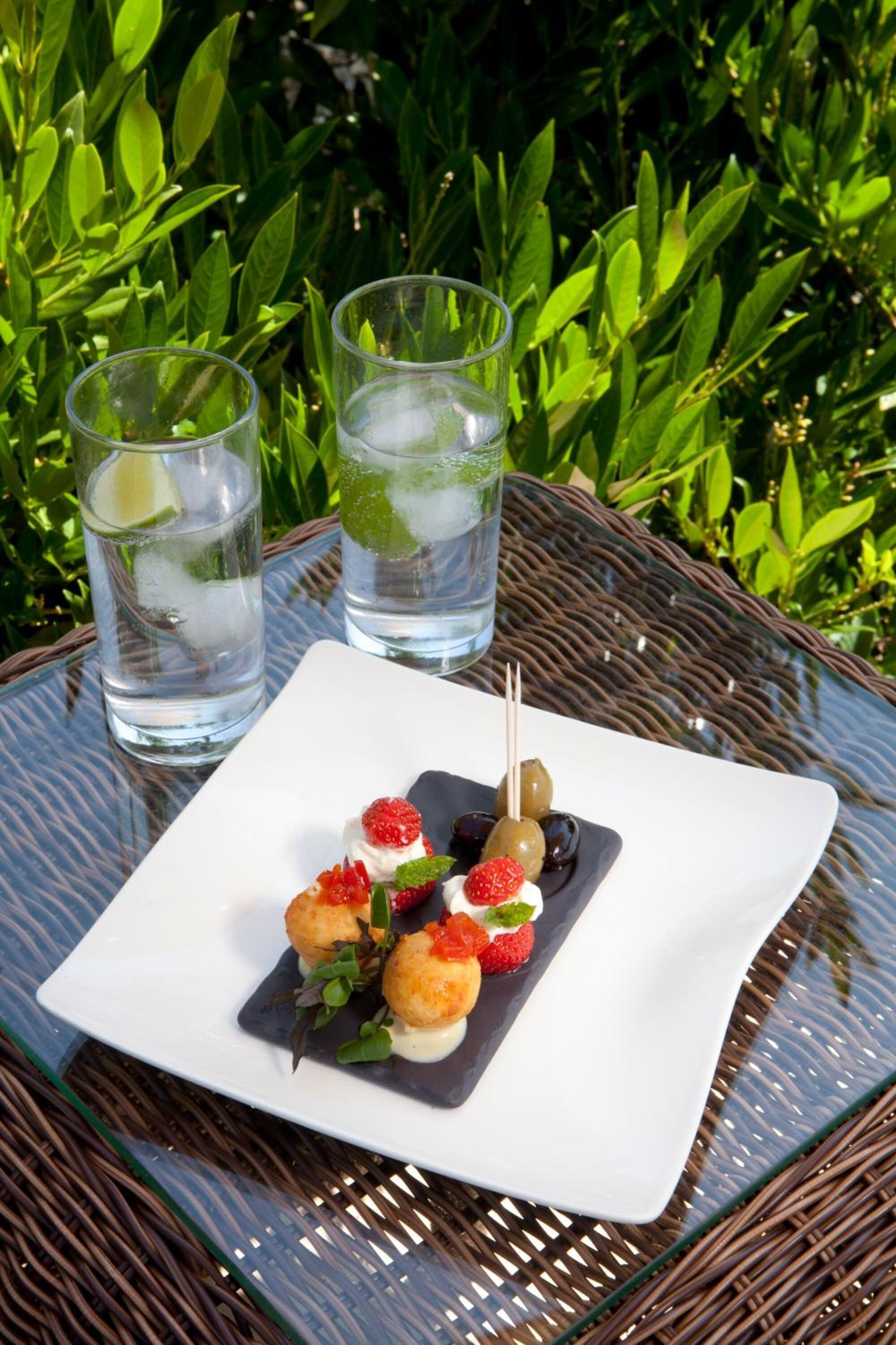A square white plate with food items on a glass table outdoors.