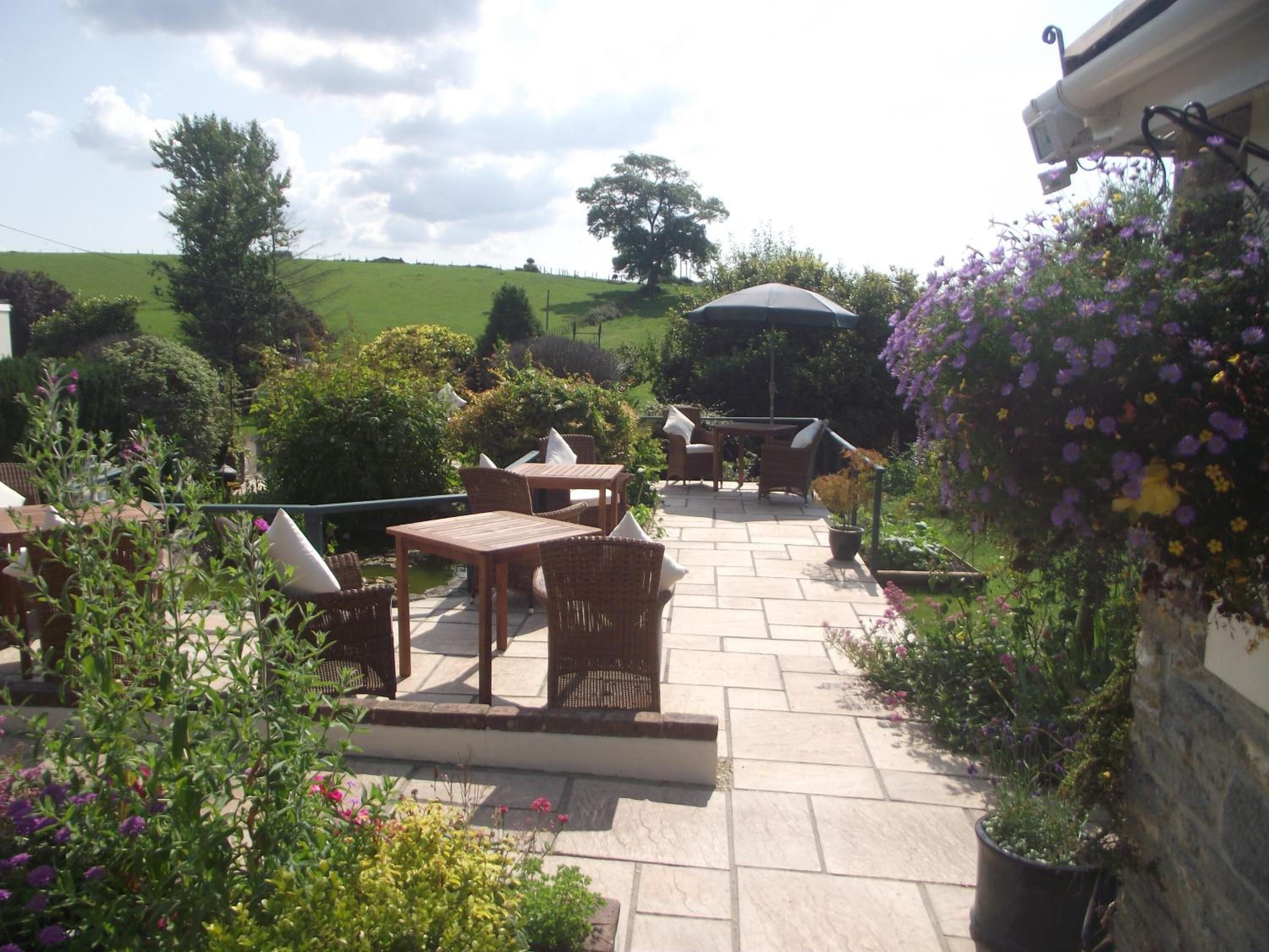 Un espace extérieur aménagé en terrasse, avec des tables et des chaises, entouré de plantes et de fleurs en pot.