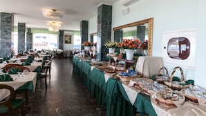A spacious dining area with marble columns, green tablecloths, and a variety of food and drink displays. - Hotel Negresco (Cervia)