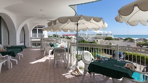 An outdoor patio with white chairs and tables, covered by large umbrellas, overlooking a pool and a view of the sea. - Hotel Negresco (Cervia)