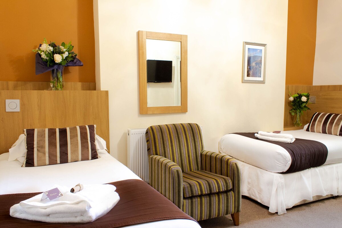 Habitación de hotel con dos camas, una silla, un espejo y un ramo de flores.