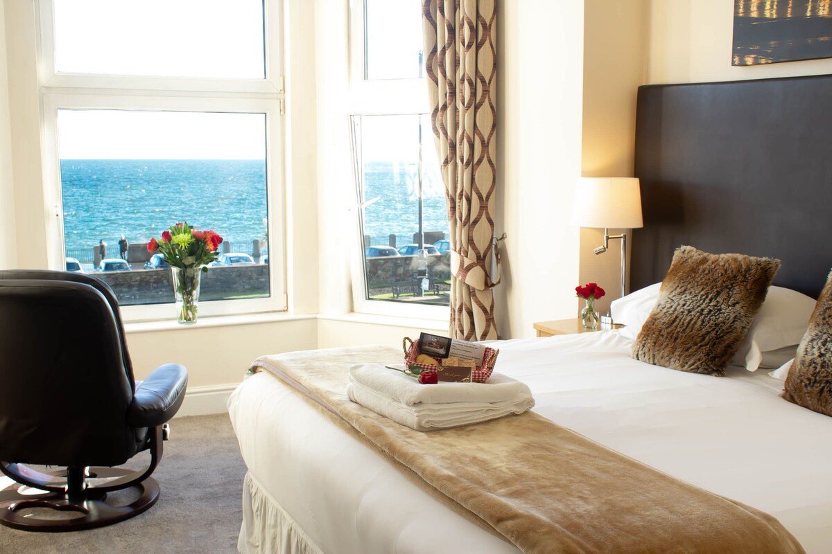 Habitación de hotel con cama, una silla, ventana con vista al mar y una lámpara.