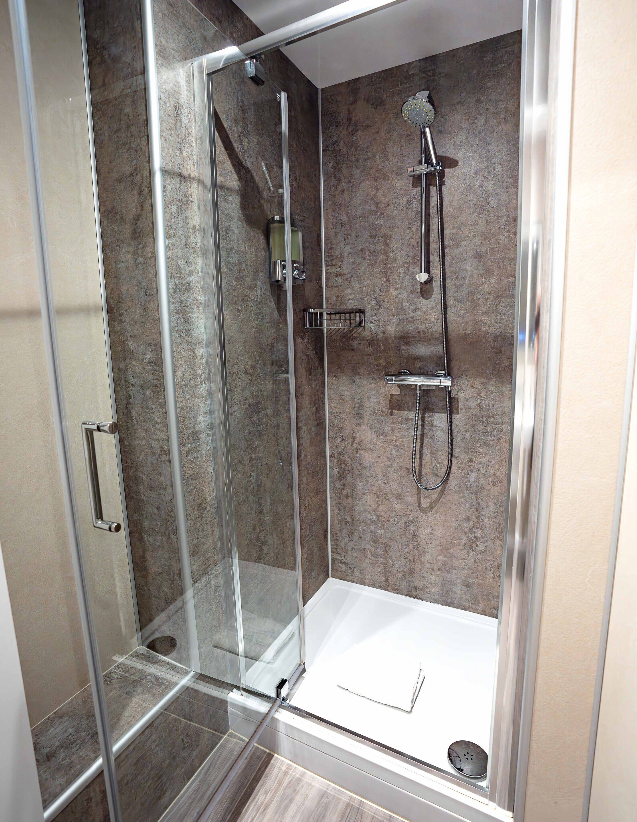 Une cabine de douche moderne dotée d’une porte en verre, d’un pommeau de douche à main et d’un robinet mural.