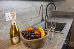 A kitchen counter with a bottle of champagne, a wooden bowl of fruit, and two glasses. - Amadeus Apartments (Douglas)