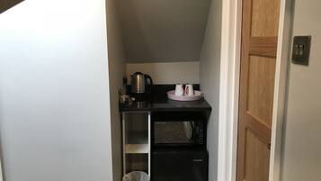Una cocina compacta con microondas, cafetera y cubo de basura.