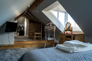Ein Schlafzimmer mit schrägverdeckter Decke, einem Bett, einer Holzkommode, einem Stuhl und einem Schreibtisch mit Stuhl.