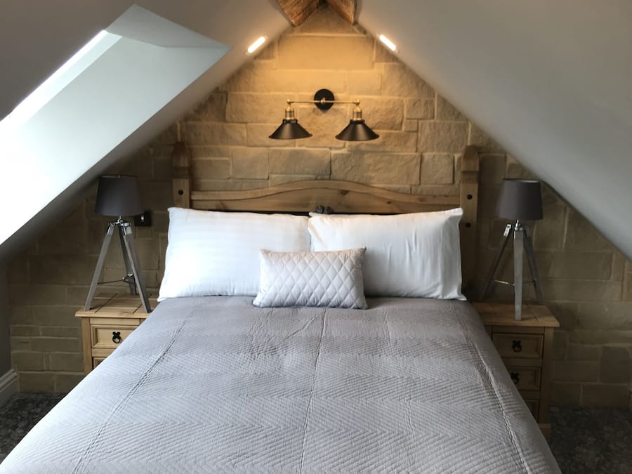 Un dormitorio con techo abovedado, una cama con manta acolchada, dos lámparas de noche y una pared de piedra.