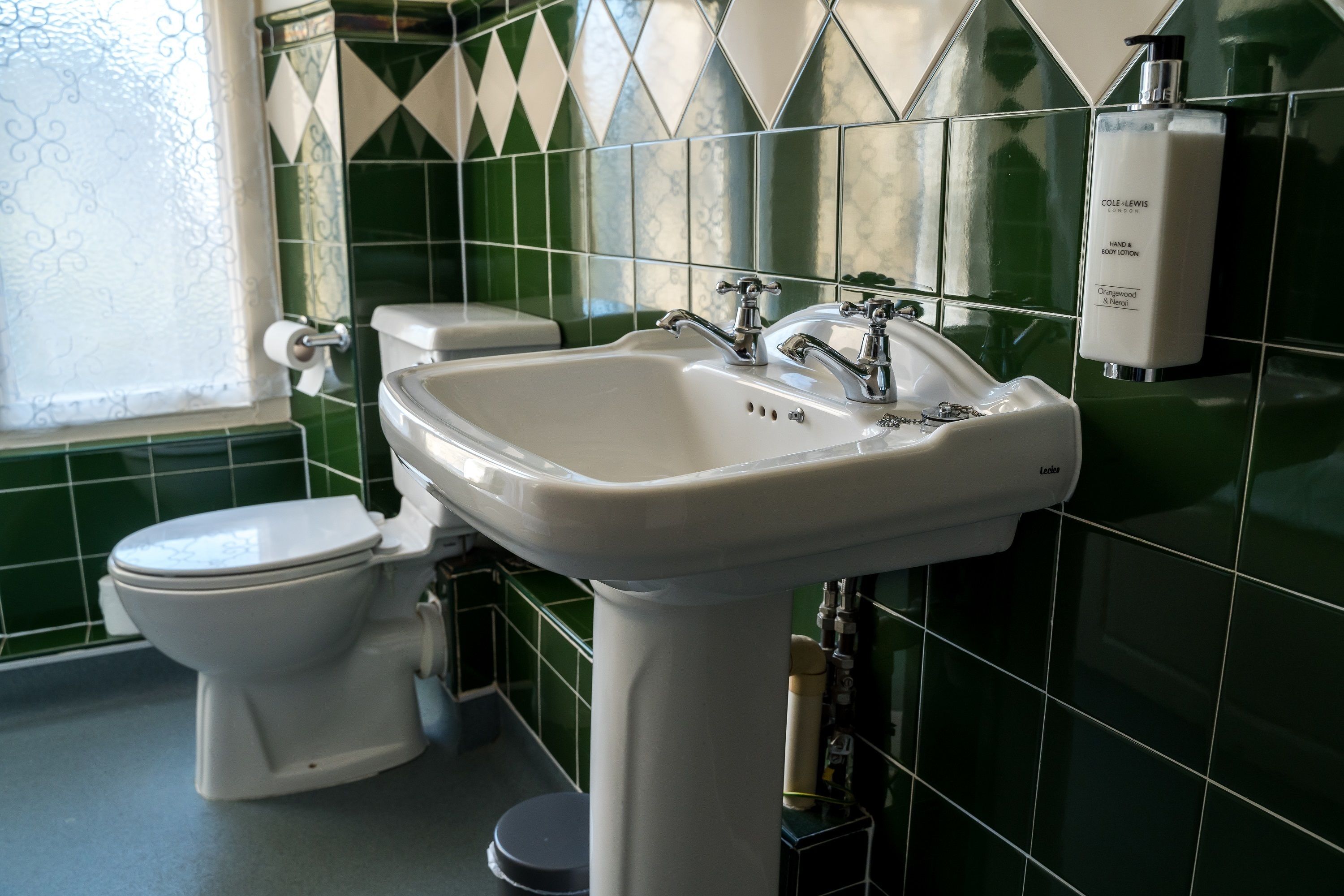 A bathroom with a white sink, a toilet, and green tiles.